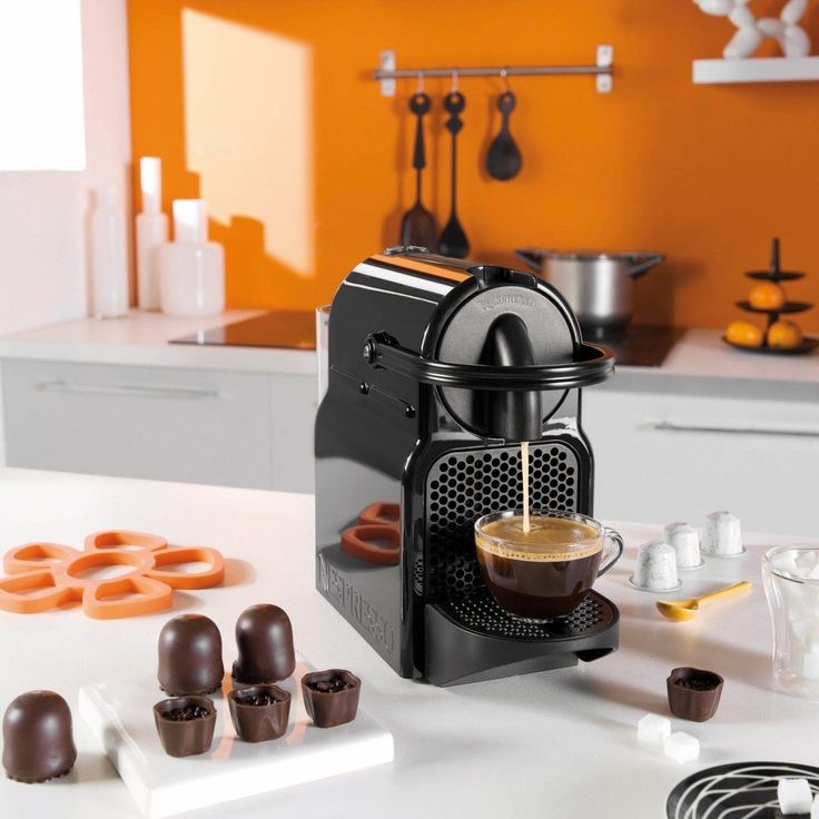 une machine a café nespresso inissia krups noir sur un meuble de cuisine avec une tasse de café remplie 